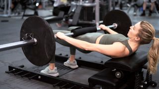 Woman performing hip row with barbell in gym on bench